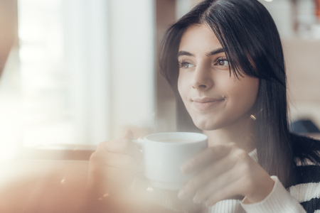 Beautiful caucasian girl in casual clothes smiling while sitting in cafe. Warm moodの写真素材