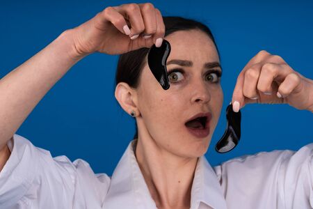A girl in home clothes without makeup removes patches, it looks strange and she expresses the...