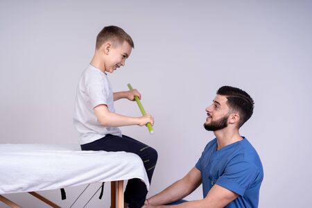 Cute boy sits on a special couch, beside him, sat the doctor in the form of doctors, concept of treatment and rehabilitationの写真素材