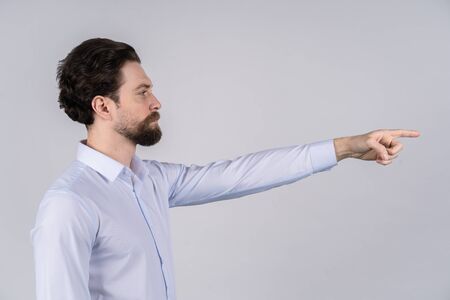 A man with a beard in a white shirt standing on white background and pointing in the directionの写真素材