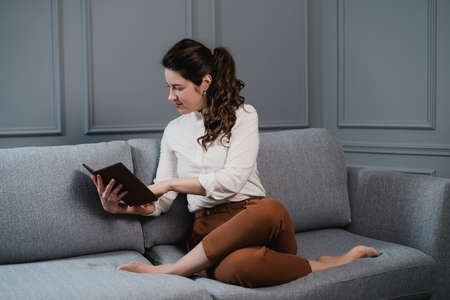 Girl reads a book in her spare time sitting on the couch. Reading a book between work.