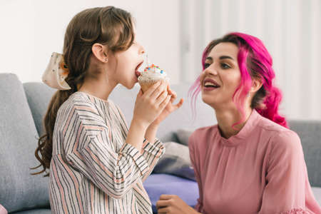 girl enjoys the taste of sweet cupcake while her mom watches her with a smile on her faceの写真素材
