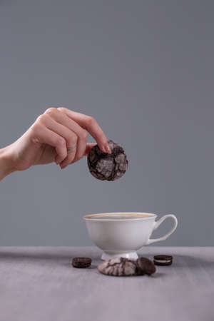 Cup of cappuccino on the table. The girl holds a cookie over a cup. Coffee with pastries is tastier.