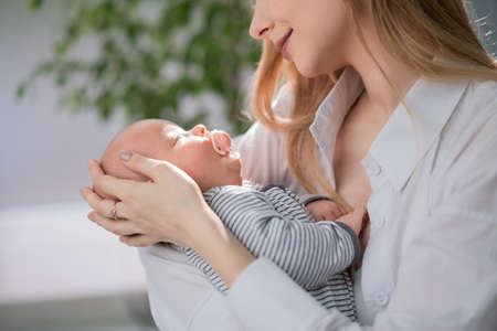 A young mother carefully holds the baby and admires him. Mothers love for her child.の写真素材