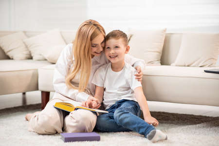 Mom and son sitting on the floor and reading a book. Time spent with benefit.の写真素材
