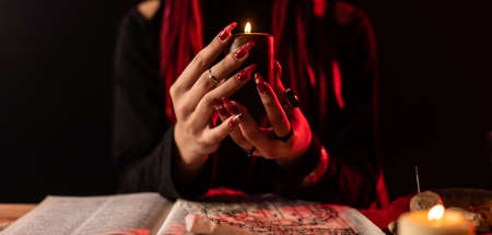 A witch who performs a ritual with a candle. Candle in female hands with red long nails.の写真素材