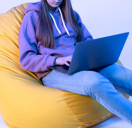 Girl looking at laptop holding hands on it. Dressed in jeans and a pink jacket. Photo details.の写真素材