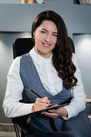 Portrait photo of a girl in business clothes. Beautiful girl in office style sitting on a chair.の写真素材