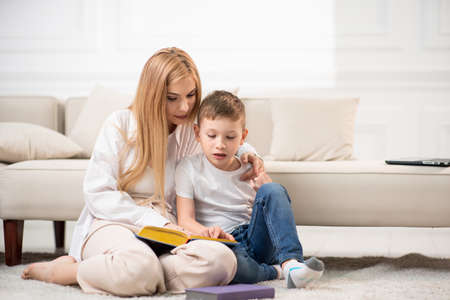 The mother reads the book and the son listens attentively. Mom spends time for the benefit of her son.の写真素材