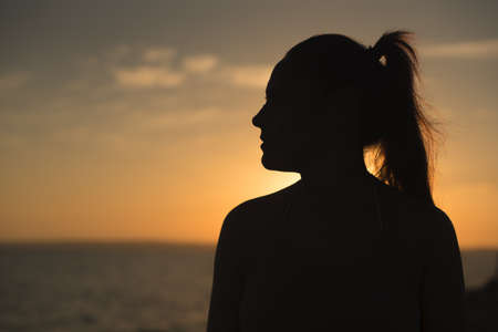 Backlit profile of a pretty woman looking at a beautiful sunset by the sea. Formentera island, Spain.の写真素材