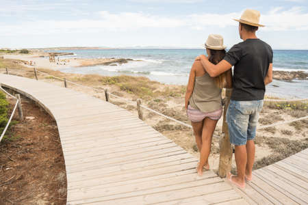 Couple of man and woman in love walking along a path of wooden boards by the sea. Long shot. Formentera island, Spain.の写真素材