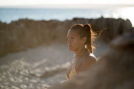 Close-up of pretty woman against the light in bikini looking to the side on a beach with the sea in...