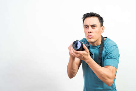 Man with photo camera photographing something very concentrated, looking straight ahead. Mid shot. White background.の写真素材
