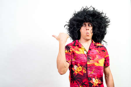 Man in afro wig and hawaiian shirt, pointing aside very surprised. Mid shot. White background.の写真素材