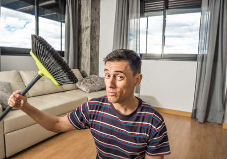 Man in casual clothes sweeping his living room. Mid shot.の写真素材