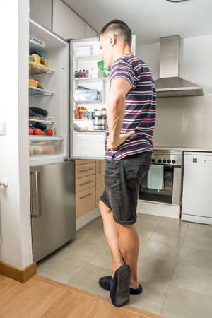 Man in shirt and slippers looking thoughtful inside the fridge. Full body.の写真素材