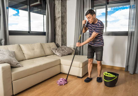 Man in casual clothes and slippers mopping the living room floor. Full body.の写真素材