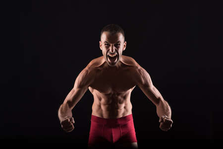 Furious shirtless man showing his muscles. Mid shot. Black background.の写真素材