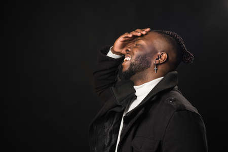 Black man in profile laughing with his hand on his face.の写真素材