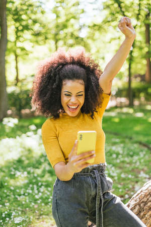 Pretty afro woman chatting on her mobile, celebrating good news.