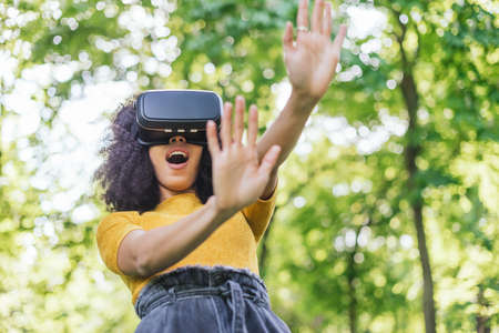 Afro woman wearing a virtual reality glasses in a garden.