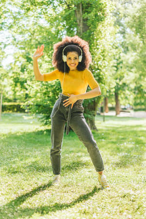 Pretty afro woman listens to music with headphones in a garden.の写真素材