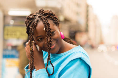 Black woman putting on her earrings in the city, smiling.の写真素材