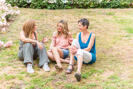 Front view of three mature women sitting in the park chattingの写真素材