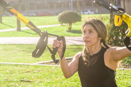 Fitness woman exercising with fitness straps in the park