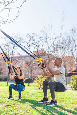 Fitness couple doing legs exercise with fitness straps in park