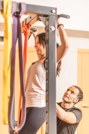 View of a athlete woman doing pull ups exercise with bar with help of trainer
