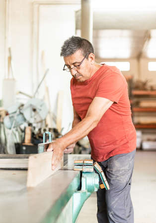 Adult man focused working manually with a wood planing machineの写真素材
