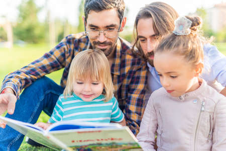 gay male couple with their children reading a book.の写真素材
