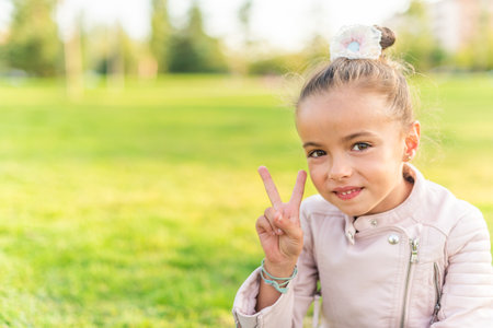 little girl sitting on grass showing peace or victory sign
