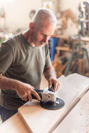 Person operating with a hand sander over a wooden boardの写真素材