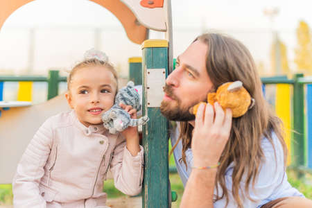 girl and father playing with stuffed animals using as phones.の写真素材