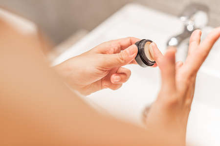 Hands of woman holding pot of anti-dark circles cream.