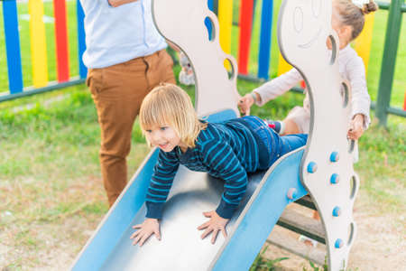 Little boy playing slider at playground with his little sisterの写真素材