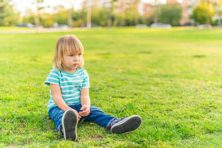 little boy sitting on grass of a park looking awayの写真素材