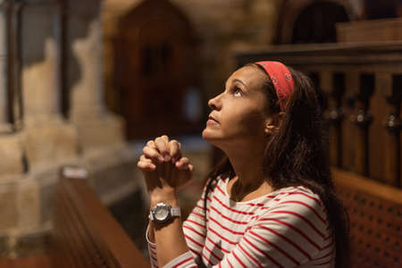 Hispanic woman praying with clasped hands in cathedralの写真素材
