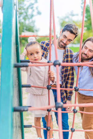 Girl in playground with her parents looking at camera unhappy.