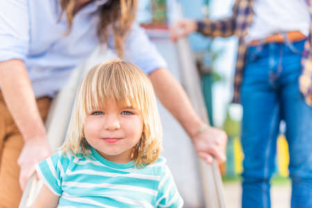 Boy looking at camera with his unrecognizable dads behind him.の写真素材