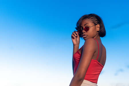 Black young woman posing confident holding a sunglasses during duskの写真素材