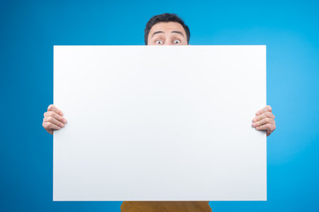 Surprised man covering half of face with blank bannerの写真素材