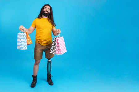 Smiling man with prosthetic leg holing many shopping bagsの写真素材