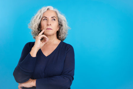 Mature woman gesturing and looking up with thoughtful expressionの写真素材