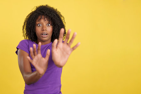 Woman with afro hair expressing fear while shielding with handsの写真素材