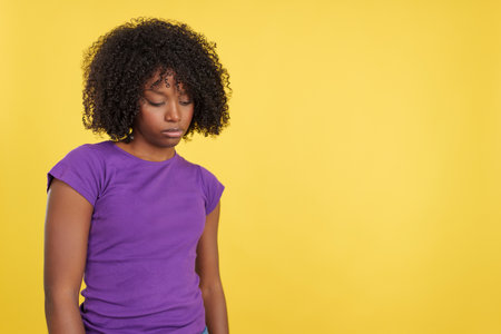 Woman with afro hair looking down with sad expressionの写真素材