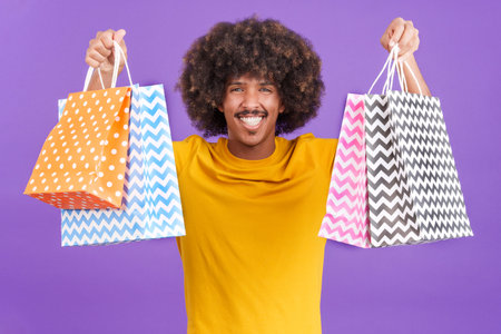 African man smiling at the camera while showing shopping bagsの写真素材