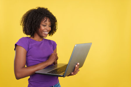 Woman with afro hairstyle smiling while using a laptopの写真素材